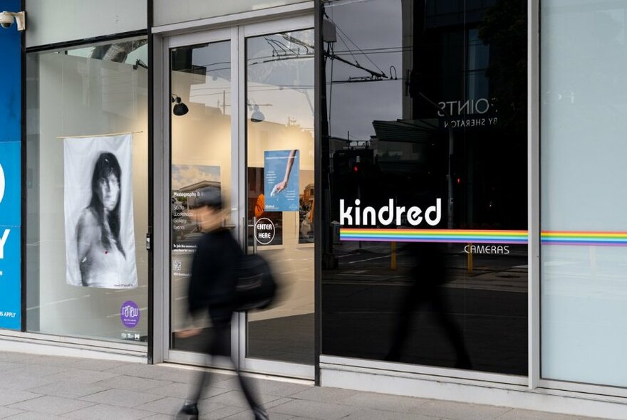 Person walking by the exterior of a building with the words 'kindred' written on the darkened window.