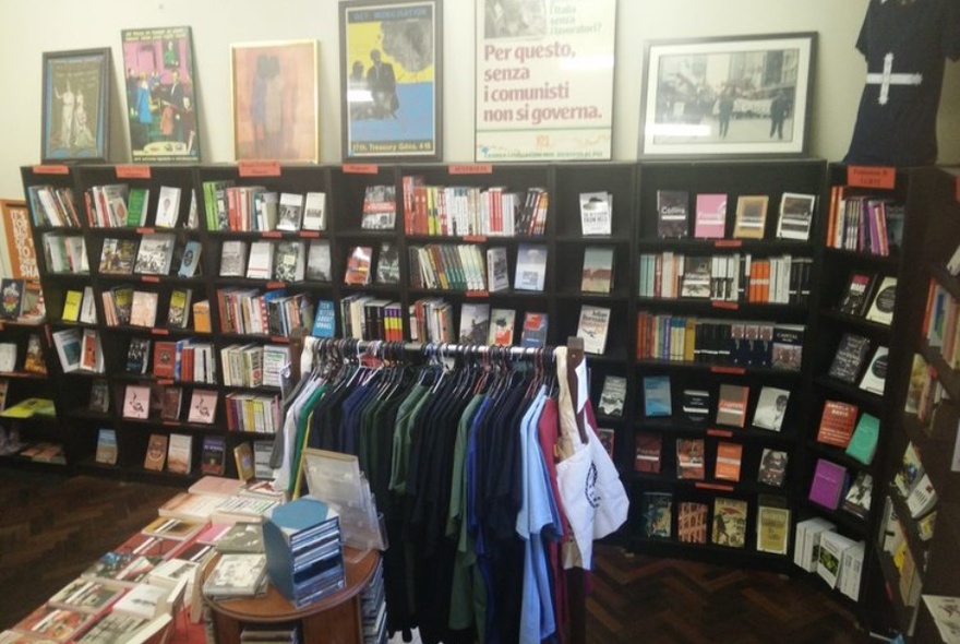 Interior of New International Bookshop, with bookshelves and display table and rack of clothes in centre.