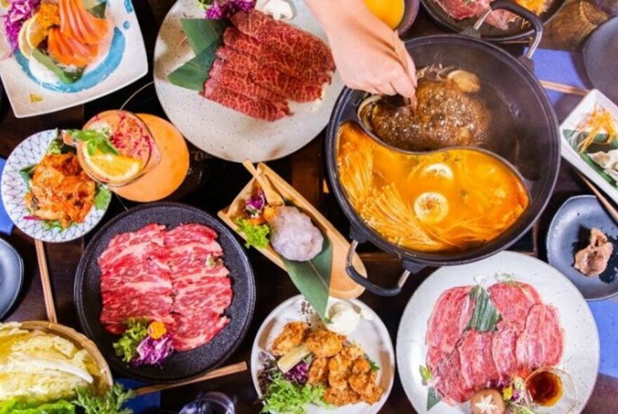 Restaurant table with raw meat and vegetables and a Japanese-style hotpot.