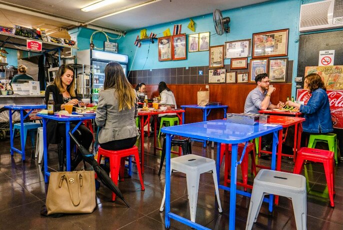 A busy restaurant with brightly coloured tables and stools.