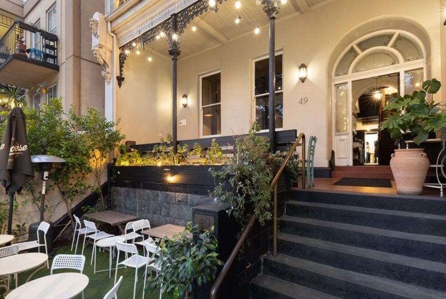 The terrace building exterior of Epocha restaurant with steps leading to a large arched doorway, and a few tables and chairs in a front courtyard space.