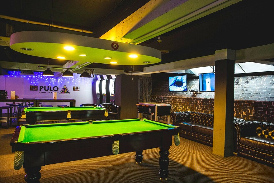 Two billiard tables in a large room, with leather chesterfield couches against the walls.