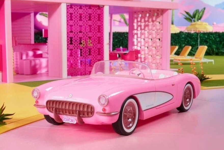 Barbie roofless corvette toy parked in front of Barbie's dreamhouse.