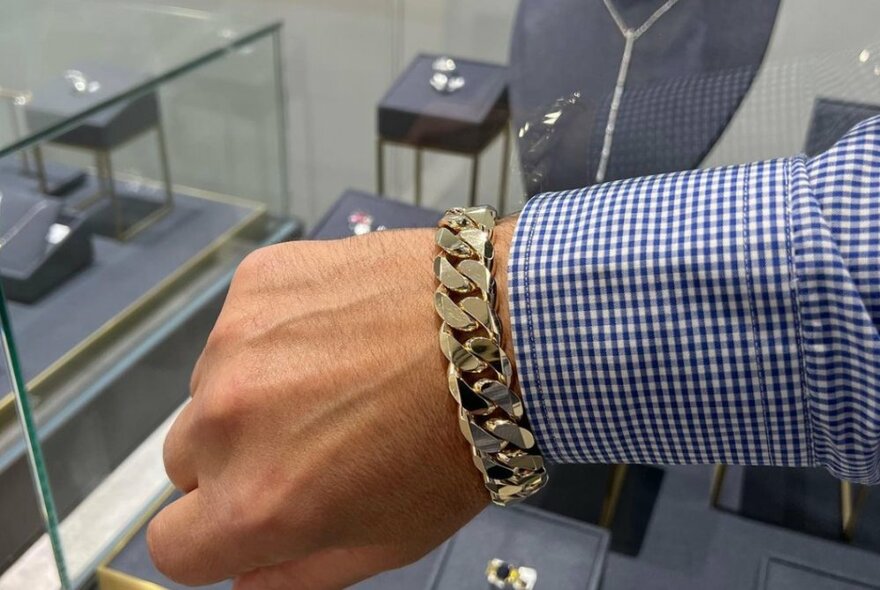 A heavy gold link bracelet worn around a man's wrist, with a shirt cuff just touching it.