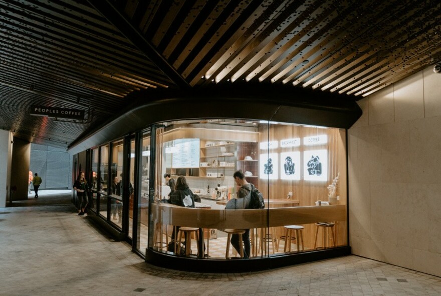 Exterior of People's Coffee: wooden benches and chairs seen through curved glass.