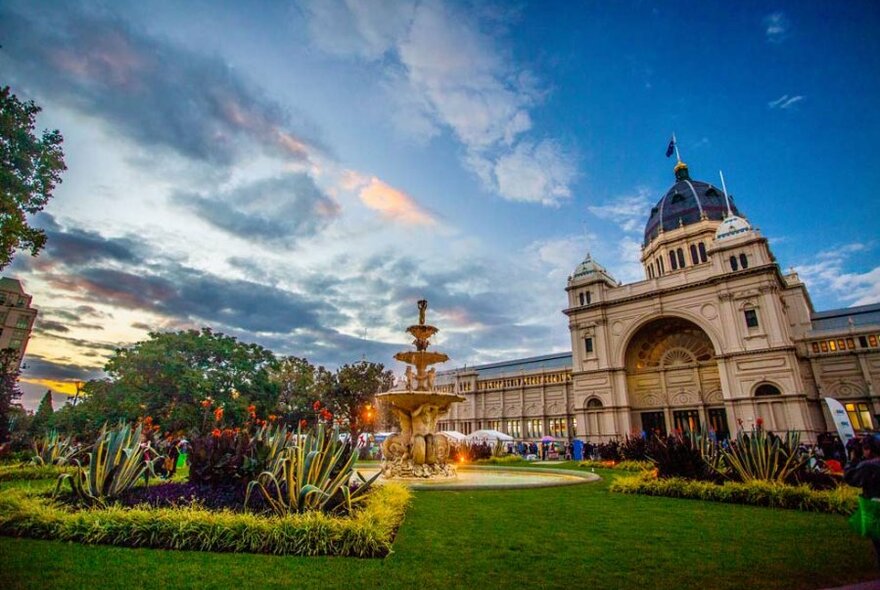 A tall heritage building in a lush green garden at sunset