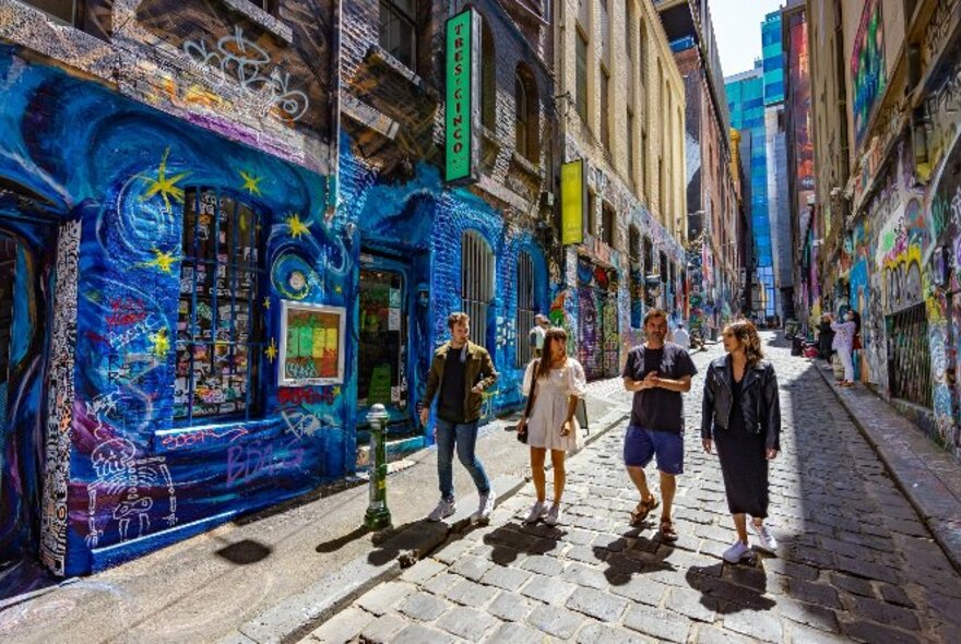Four people walking down an alley covered in street art. 