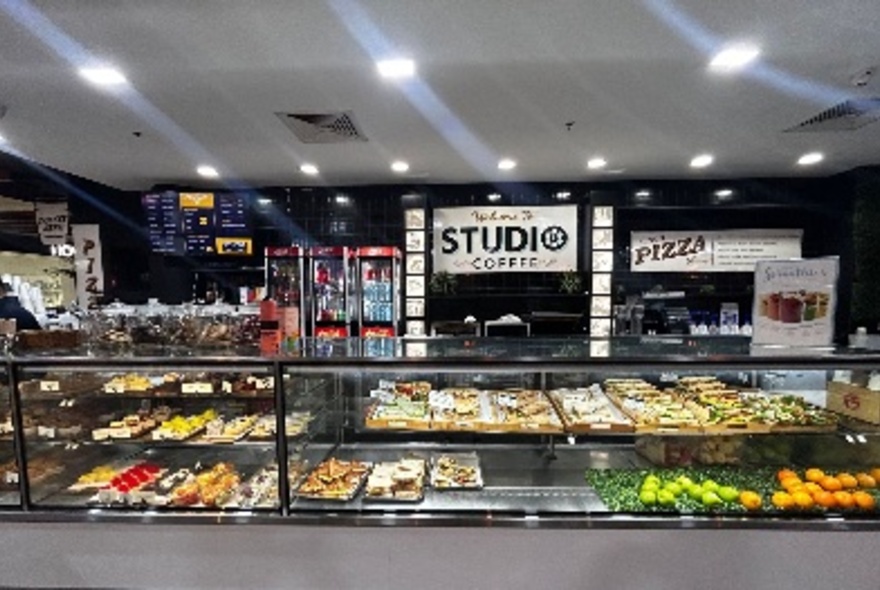 Exterior of Studio Coffee showing glass display cabinets at front filled with pre-made food, and signage and a drinks fridge on the rear wall.