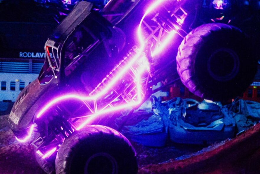 A neon illuminated monster truck with oversize tyres on display in a stadium.