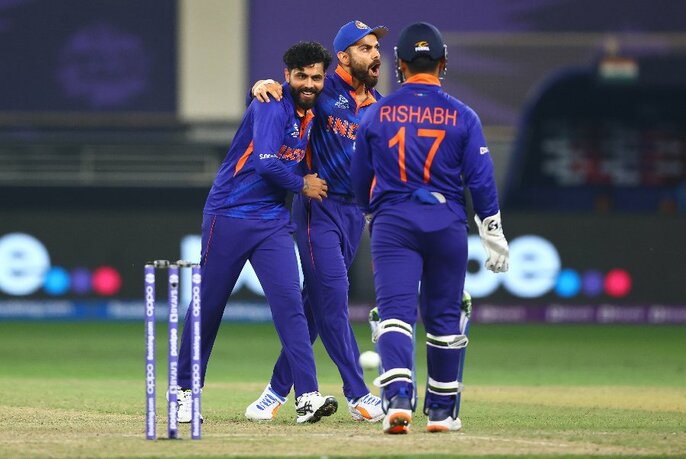 Three members of the Indian T20 men's cricket team wearing their distinctive royal blue uniforms, on the cricket field.