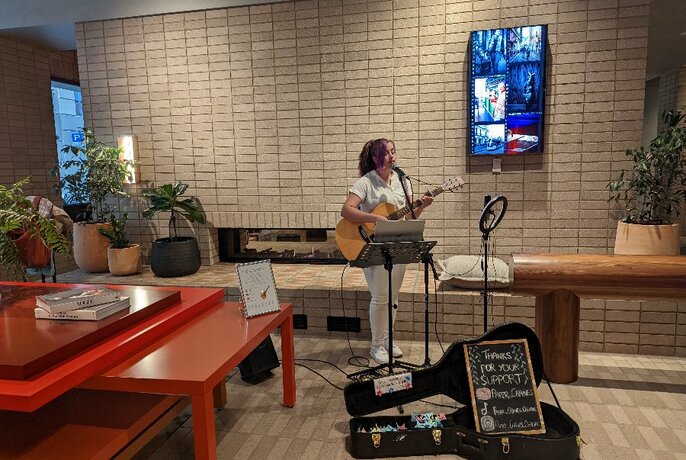 Busker performing with open guitar case in hotel foyer with tables and decor.