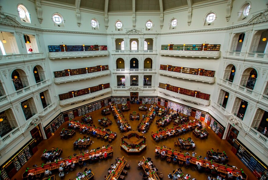 People seated at desks arranged in an octagonal pattern inside the La Trobe Reading Room of State Library Victoria.