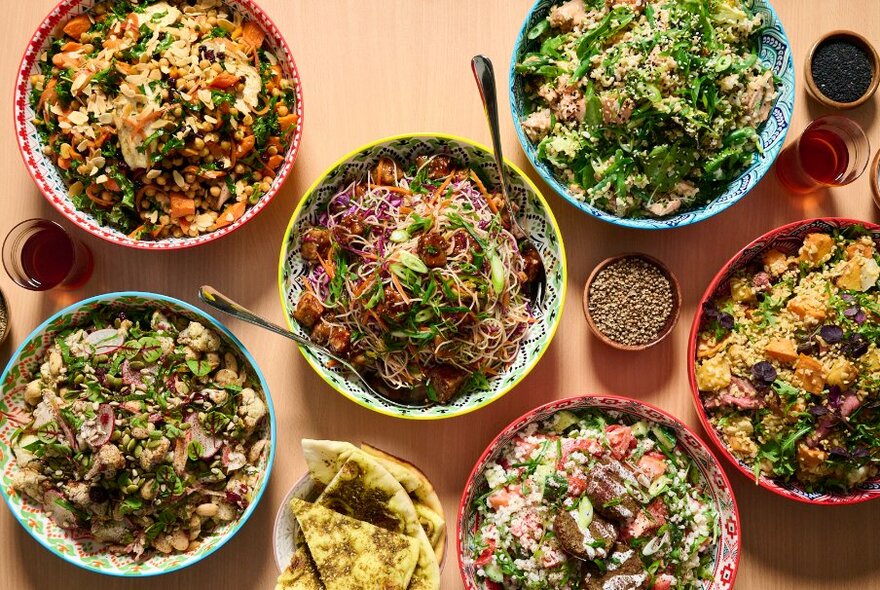Overhead view of assorted salads and vegetable dishes in large bowls on a table.