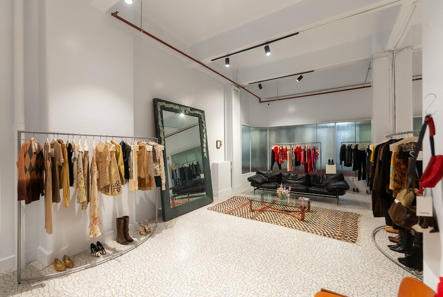 A minimalist boutique with a large mirror and racks of vintage clothing. 