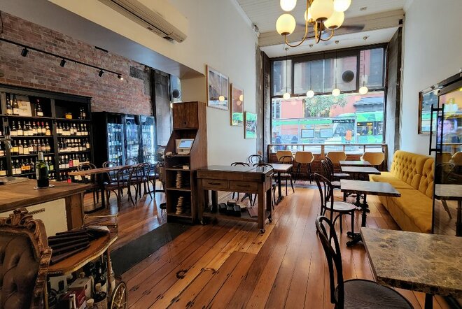 Interior of V Wine Salon showing shelves of wine, tables, chairs, velvet banquette seating against the wall, with a view out the window onto a city street.