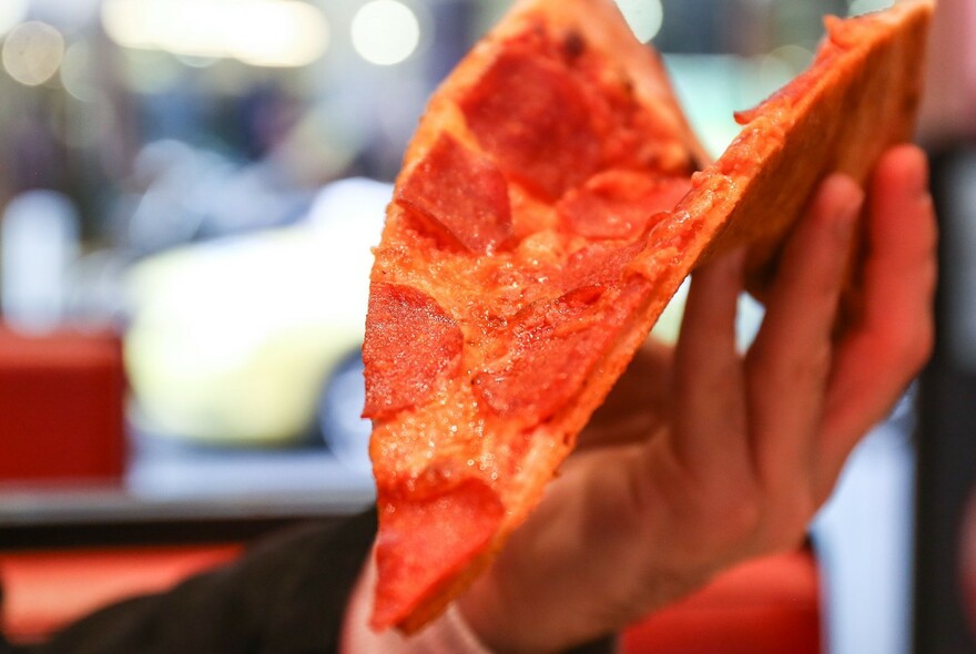 Hand folding a large slice of pepperoni pizza.