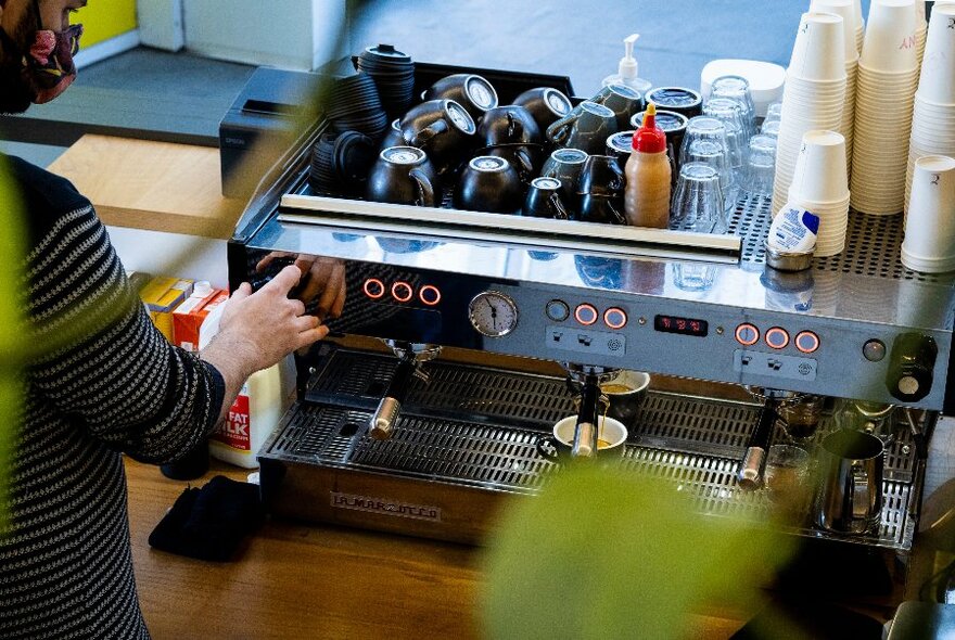 Looking on an angle over the shoulder of a barista as they use a large coffee machine. 