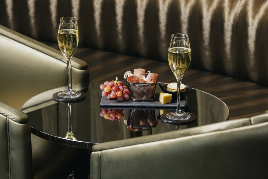 Banquette and bar table with two glasses of wine and antipasto platter with grapes and cheese.