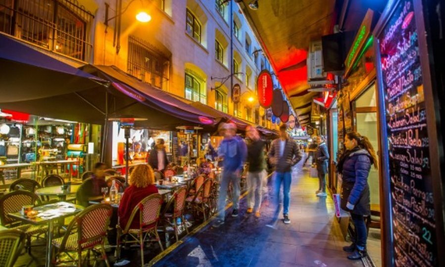 A busy laneway at night with dining in the centre, pedestrians and neon lights 