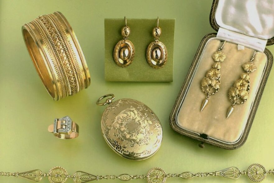 Gold jewellery resting on pale green fabric, including bange, earrings, bracelet and ring.