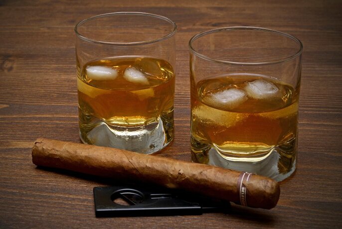 Two glasses of spirits with ice, plus a cigar.