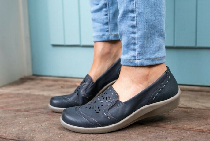 Model's feet with jeans and rubber-soled comfortable leather slip-ons with perforated design.