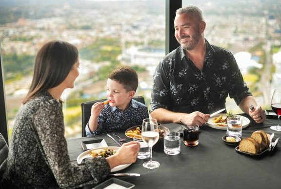 Parents and child dining at a table with soaring panoramic views of Melbourne.
