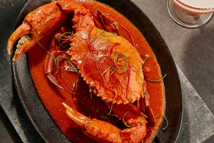 A whole cooked crab with a red sauce on a black plate.