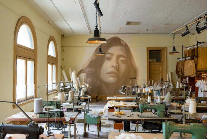 A room full of old Singer sewing machines with a mural of a woman's face on the wall.