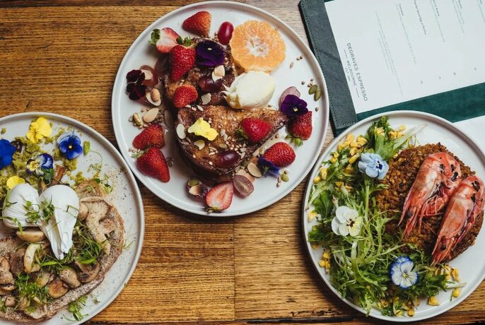 Overhead view of three plates of delicately arranged food on white plates, with a menu partially visible in the top right corner.