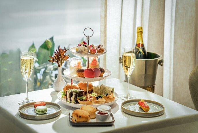 Three-tiered display stand of savoury and sweet food and glasses of champagne, as you'd find at a high tea.