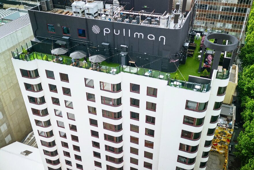 Aerial view of the Pullman Melbourne City Centre, a white high rise building in the centre of the city, with a rooftop bar visible.