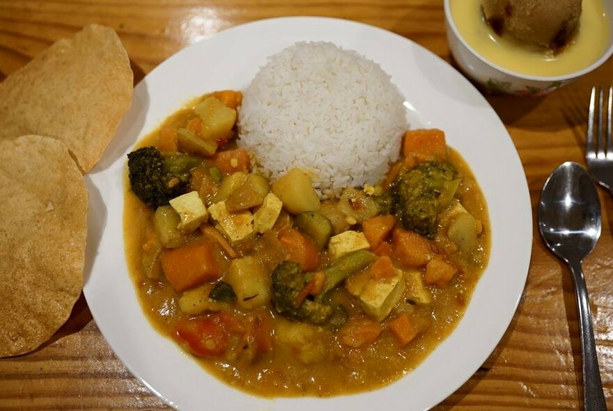 A plate of vegetarian curry and rice, with pappadams on the side and cutlery