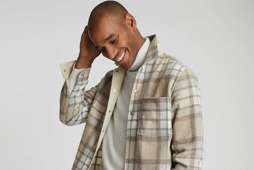 Model with dark, shaved hair, in cream and light brown plaid shirt and cream skivvy.