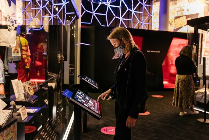 A museum visitor in an exhibition space using a screen, surrounded by display objects.
