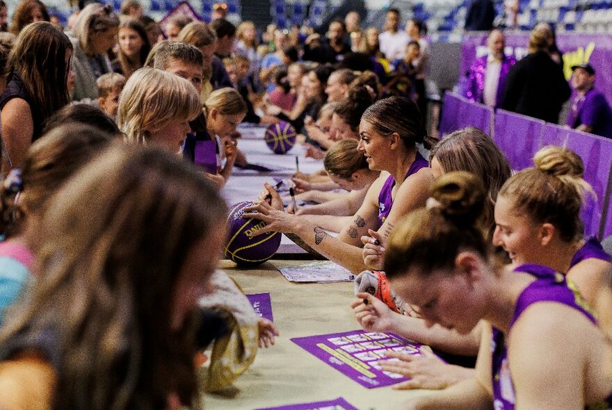 Players from the Melbourne Boomers basketball team interacting with their fans at a table and signing autographs and merchandise.