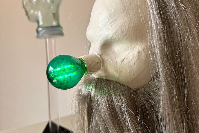 Bright green light globe attached to a plaster sculpted object that has a silver grey hair wig attached.