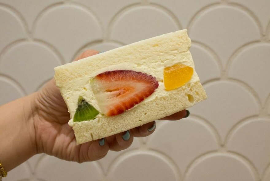 Hand holding fruity cream sando on it's side, showing inside filled with cream and fruit