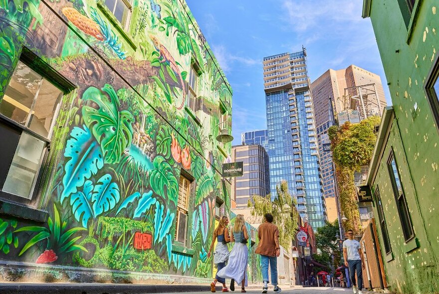 People walking down a laneway past a giant leafy jungle mural.