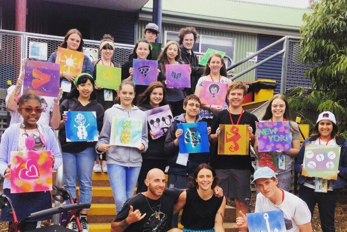 Group of smiling young teenagers holding up their canvas stencil artworks.