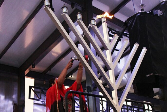 A person lighting a large silver menorah. 