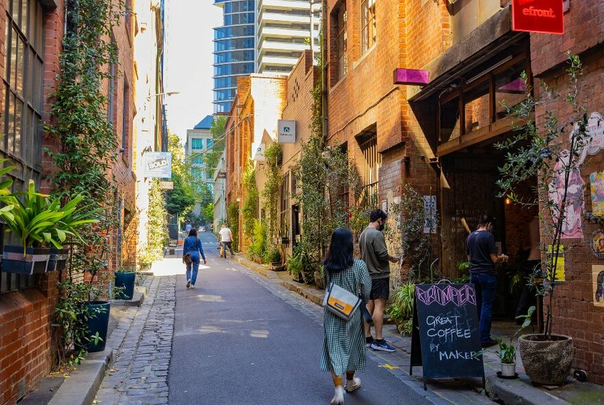 People walking down a leafy city laneway into a cafe. 
