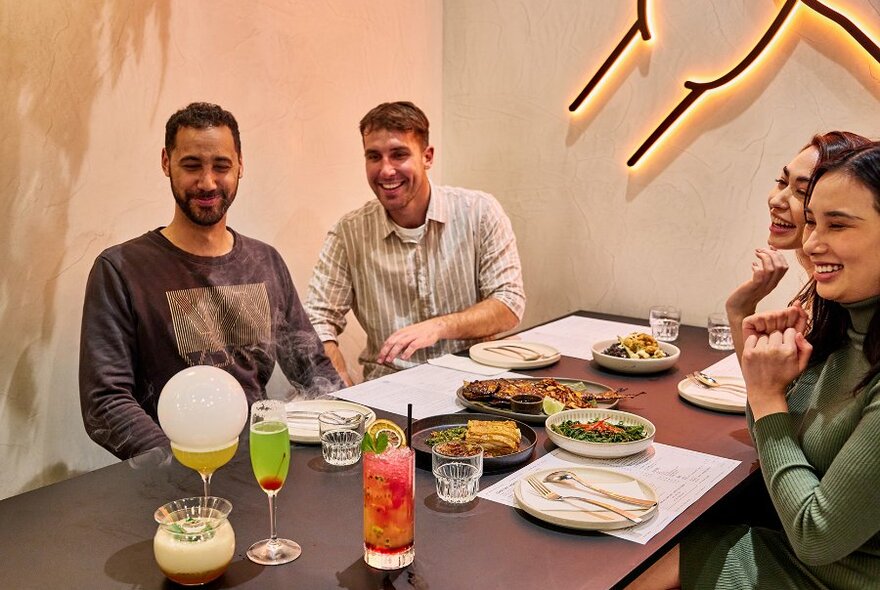 Four people dining in a restaurant on share plates and colourful drinks, including a bubble-topped cocktail.