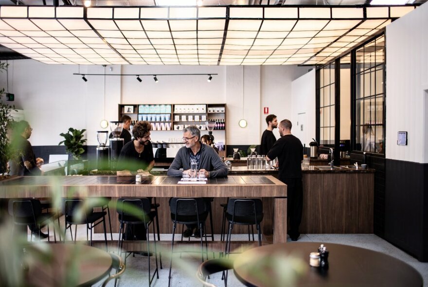 A large open plan cafe with a white and black faux ceiling and patrons on a communal table. 