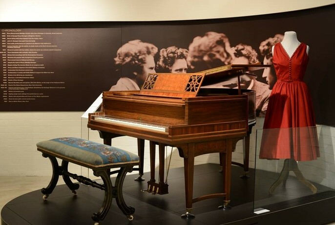 Old grand piano, seat and red dress at Grainger Museum.