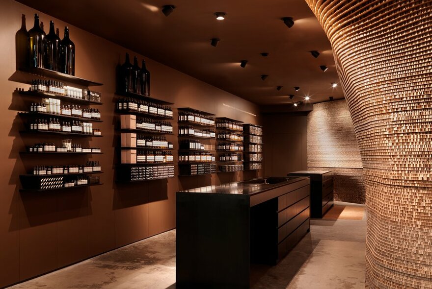 The curved wall of an Aesop shop interior with products on shelves and warm brown tones. 