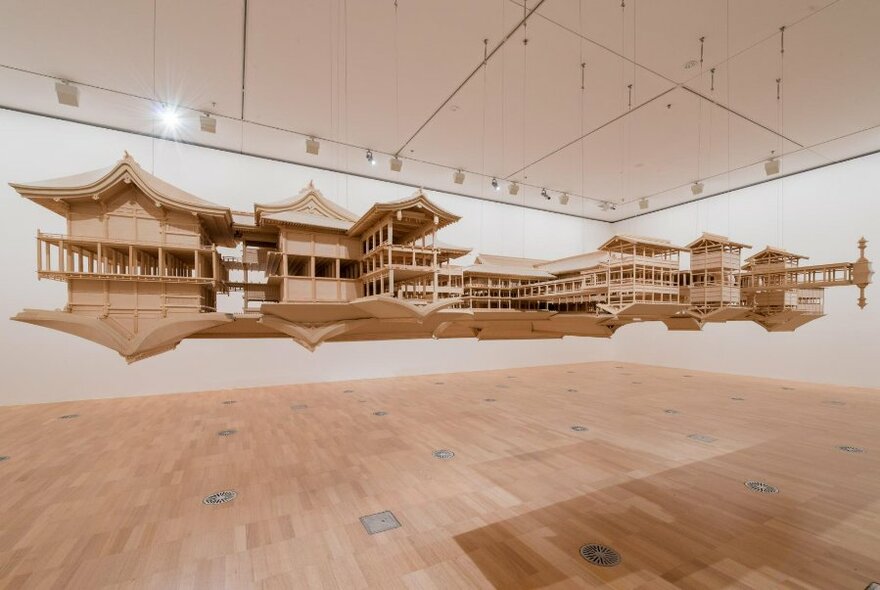 Timber small scale model of a Shinto shrine and it's reflection, hanging from a gallery ceiling, as if suspended in mid-air.