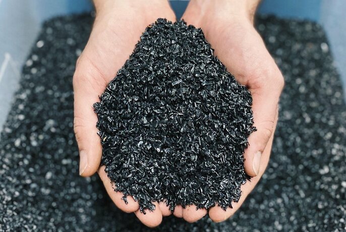 A pair of hands holding black plastic shredded for recycling.