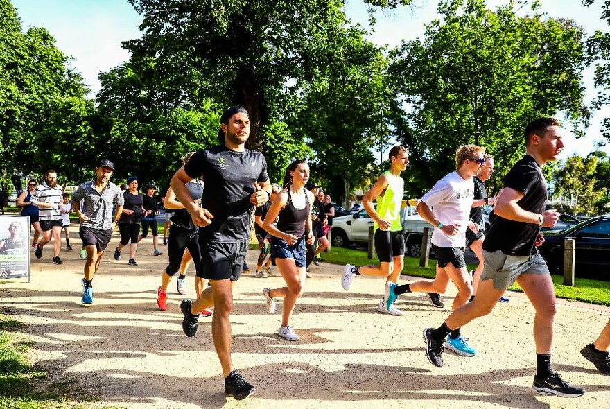 A large group of people in active wear all running on a path in park. 