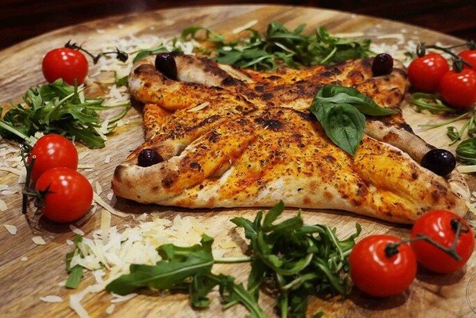 Wooden board with calzone, tomatoes, herbs and cheese.